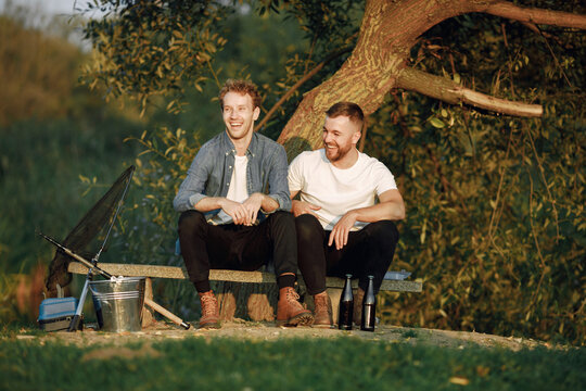 Two men fishing near the river and drinking a beer