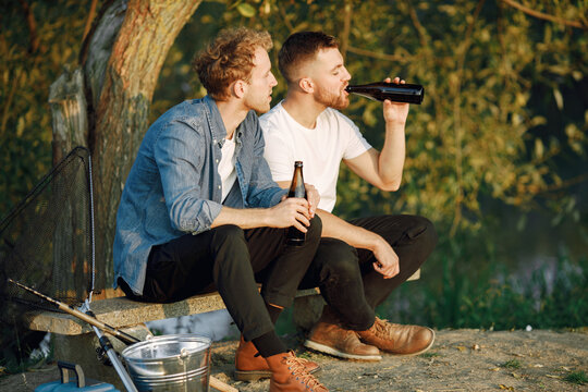Two men fishing near the river and drinking a beer