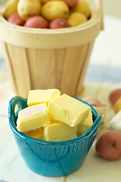 Fresh butter in a turquoise blue ramekins and a basket of small potatoes slightly blurred in the background