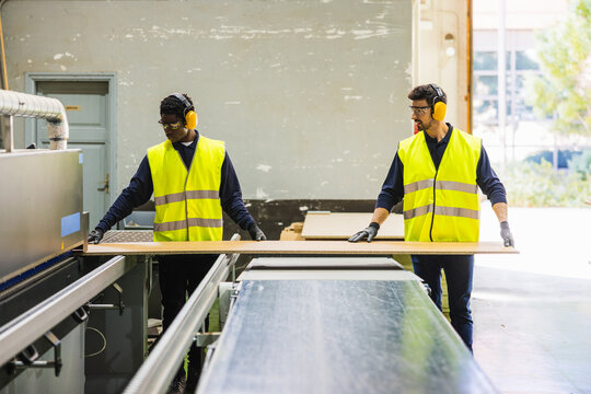 Workers processing wood panel using machinery in factory