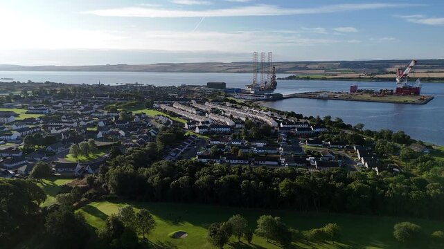 Wide aerial drone video over Invergordon town showing Cromarty Firth port with offshore oil rig and port facility in Scotland