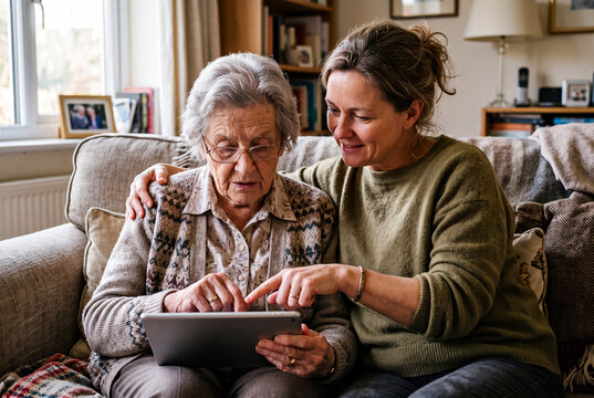 Daughter teaching senior mother using digital tablet at home