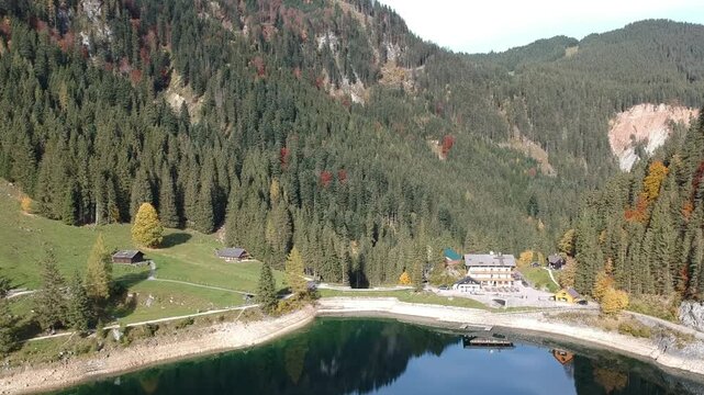 Lake Gosau Austria captured by drone with an Alpine hotel and green shoreline framed by dense forest and colourful autumn mountains in the Dachstein region.