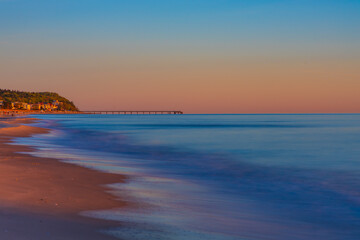 Obraz premium Panoramic View Of Empty Sandy Beach At Dawn With Distant Pier Silhouette