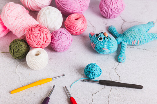 A knitted toy cat and colorful crochet balls and hooks on a table