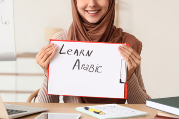 Online language learning and education, young muslim woman in hijab holding a learn arabic sign for remote classes © Pixel-Shot