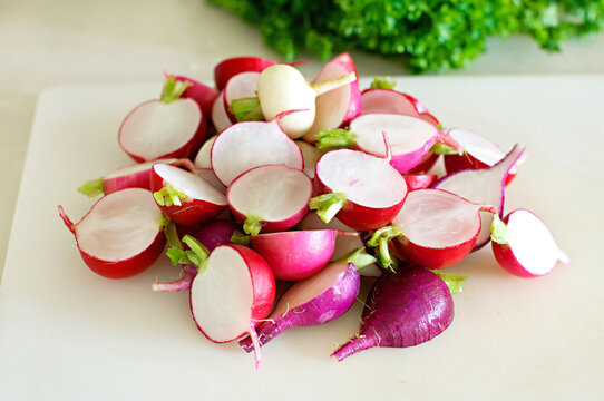 Pile of sliced rainbow radishes on a cutting board in the kitchen, with blurred parsley in the background