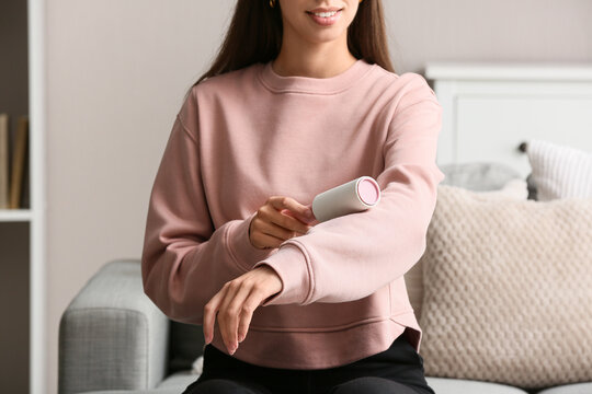 Pet hair removal and clothing care, woman using a lint roller on her pink sweatshirt at home
