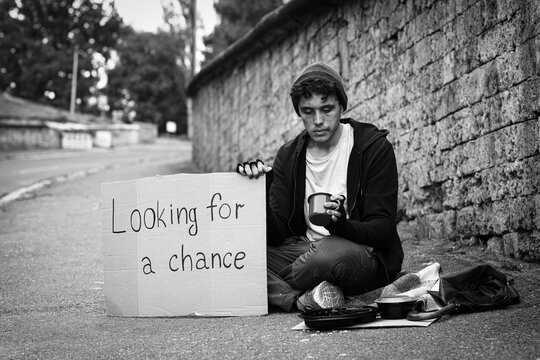 Homelessness and poverty, young man begging for help with a sign "looking for a chance" on the street