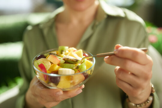 A woman in a green shirt holds a glass bowl of fresh fruit, highlighting a moment of mindful nutrition. The soft-focus home setting adds to the relaxed and wholesome atmosphere.