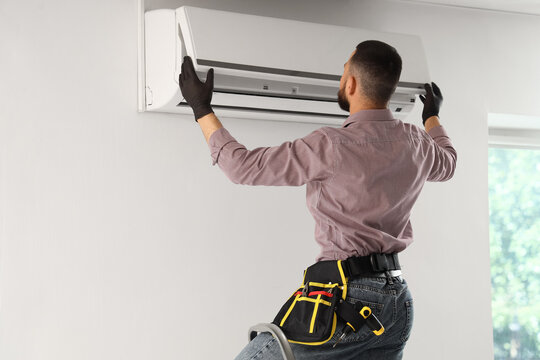 Air conditioning installation and repair service, professional technician working on wall-mounted ac unit indoors