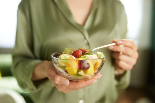 A person in an olive green shirt prepares to eat a bowl of mixed grapes, kiwi, and bananas, representing conscious nutrition and healthy home habits.