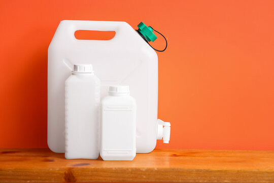 Water storage and emergency preparedness, white plastic jerry can and bottles on a wooden shelf with orange background