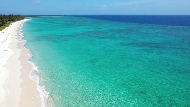 Aerial View of Pristine Tropical Beach with Turquoise Ocean Waves Lapping White Sand Shoreline Under Clear Blue Sky in a Serene Exotic Paradise Landscape during Summer