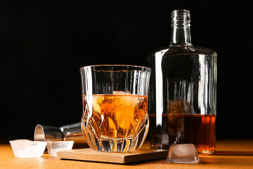 Glass and bottle of cold whiskey on wooden table against black background
