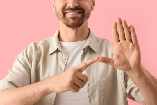 Adult man using sign language on pink background, closeup