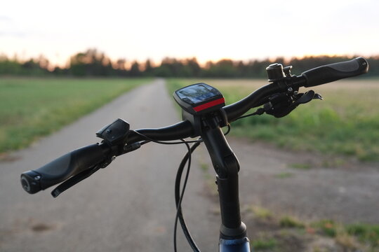 Electric bicycle handlebars and display seen in close-up on a quiet rural path at sunset, with green fields, soft evening light, blurred background and generous copy space