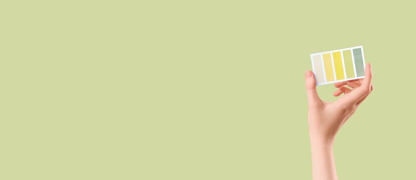 Ph balance and health monitoring, hand holding litmus paper strip with color scale on green background