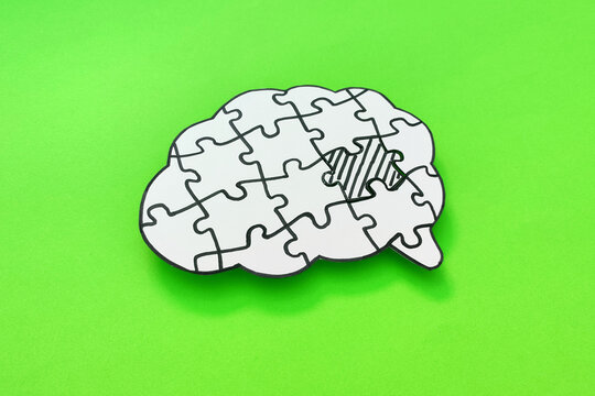 Mental health and problems with memory. Brain shaped jigsaw puzzle with missing piece on green background.