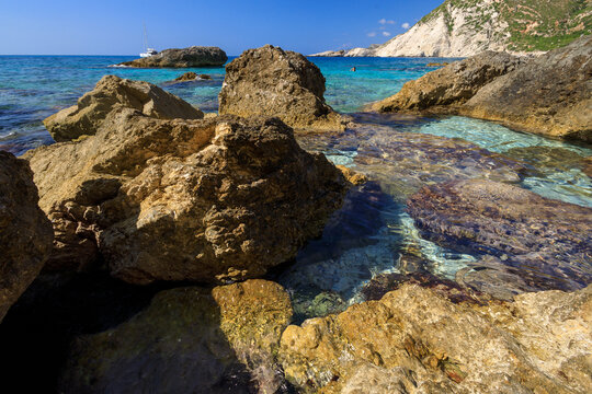 A photograph of the beautiful, azure Paralia Petani beach with large stones in the foreground.