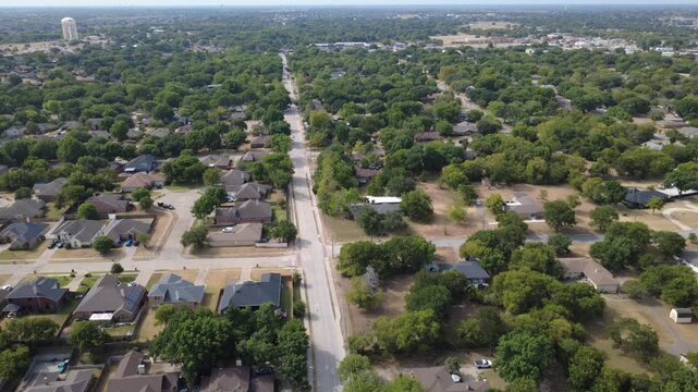 Perpendicular neighborhood cross streets divide open parcels near Ramblewood enclave. Concrete sidewalks, mature leafy trees flank single story brick family dwellings, DeSoto, Texas