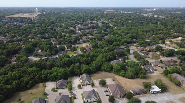 Lush tree canopy blankets natural buffer zones near Ramblewood neighborhood. Dense green foliage extends across undisturbed terrain toward distant municipal water towers, DeSoto, TX