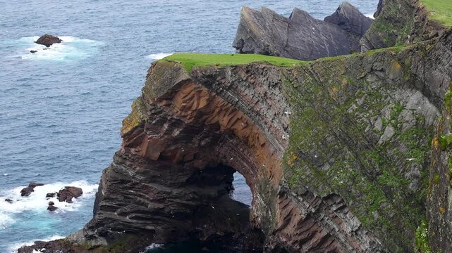 Thousands of seabirds flying around a massive sea arch below the towering cliffs of the Isle of Foula, Shetland, Scotland, United Kingdom