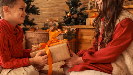 Naklejka premium Children exchanging a Christmas gift in a cozy, festive holiday setting