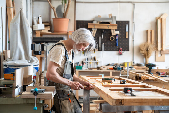 Handwork, skills and craftsmanship in restoration business, focused man restorer repairs wooden door, concentrated handicraftsman using chisel hand tool precisely carving surface, furniture renovation