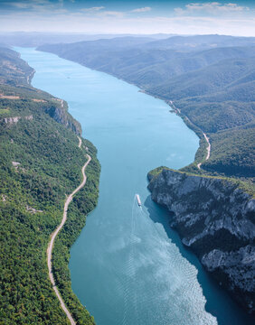 Vast forested mountain slopes framing a turquoise Danube river as a lone cruise ship navigates the winding Iron Gate gorge below. Travel concept.