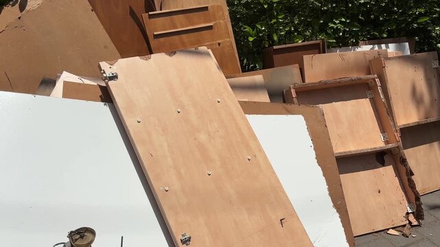Discarded household furniture placed outdoors for removal, showing dismantled cabinet doors, drawers, wooden panels and furniture parts from a home