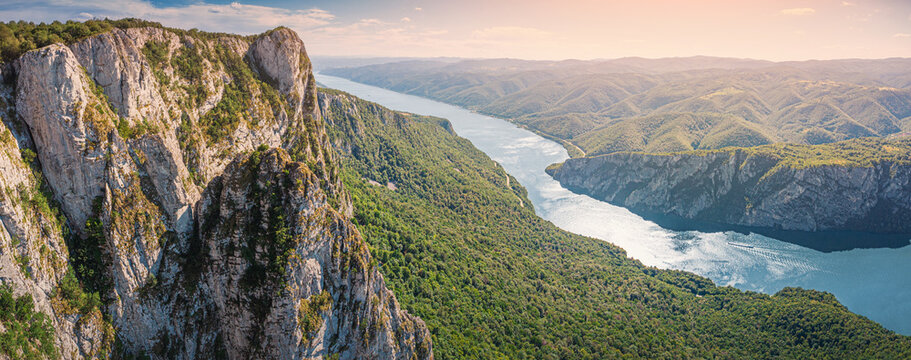 Panoramic aerial view of dramatic limestone cliffs framing a wide Danube river winding through Iron Gate gorge and valleys at sunset. Travel concept.