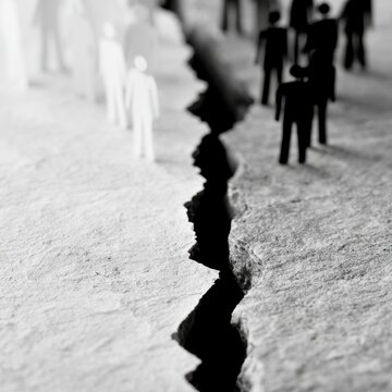 Conceptual image of division with black and white figures separated by a deep crack on a textured surface symbolizing social or ideological separation and confl