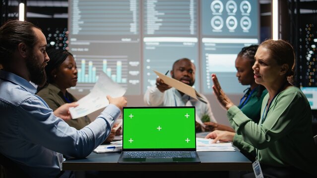 Diverse company staff hosts a late-night meeting with chroma key on a laptop, discussing budget updates, performance metrics and business objectives.