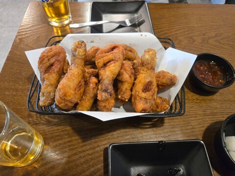 Crispy fried chicken drumsticks served in a wire basket with dipping sauce and beer
