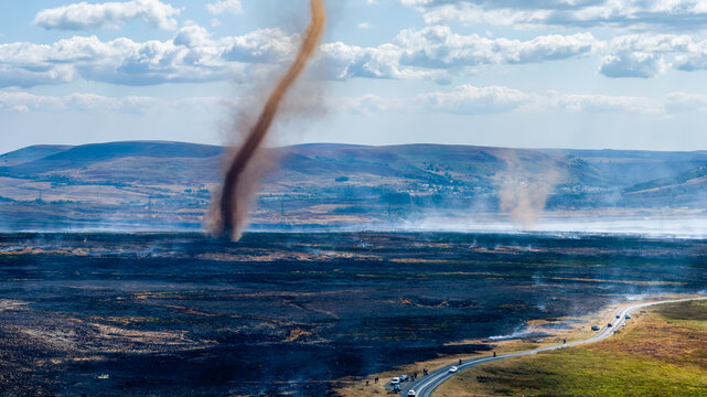 Smoke devil twisting above smouldering burnt moorland on Llangynidr Moors, smoke rising over scorched ground beside rural road in South Wales