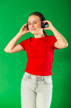 Passionate teenage girl in red T-shirt and jeans listening and dancing to music on headphones on a green background. Chroma key compositing