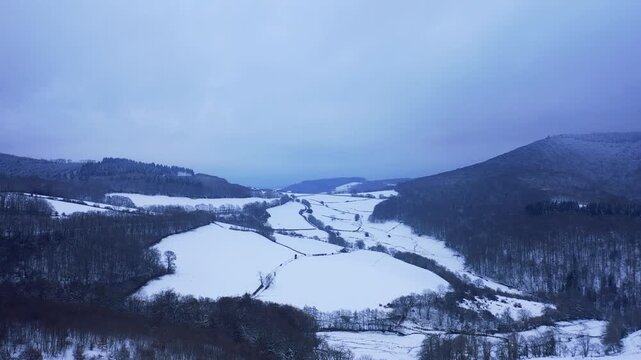A wide aerial shot of the Foret du Morvan and Haut Folin covered in snow during winter. The landscape is serene and untouched, showcasing the natural beauty of rural France under a cloudy sky.