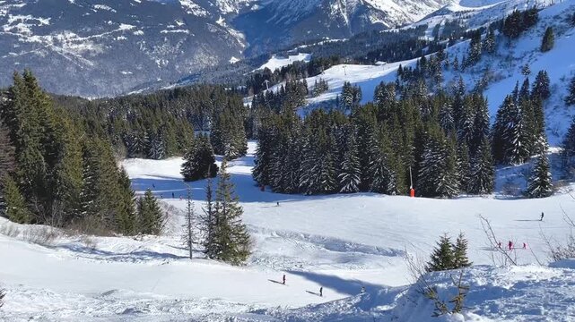 Wide view of a snowy ski slope surrounded by dense evergreen forest in Megeve, Haute-Savoie, French Alps. Captures the scenic winter sports atmosphere of this renowned Alpine resort.