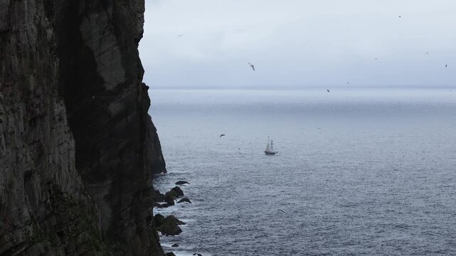 A historic wooden schooner sailing boat riding the waves below the cliffs of Foula, Shetland, Scotland