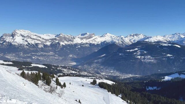 Wide panoramic view of the French Alps above Passy and Chamonix, showing snow-covered mountains, forested slopes, and a clear blue sky.