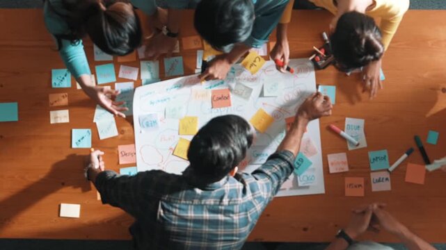 Top view of project manager writing and sticking stick notes. Aerial view of professional business people working together planning strategy while drafting mind mapping at meeting room. Symposium.