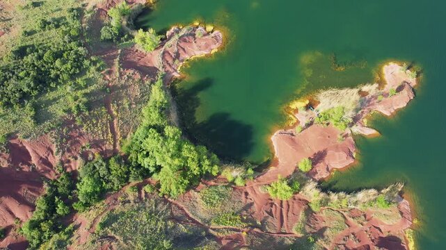 Aerial footage showing the distinctive red earth shoreline and green waters of Lac de Salagou in Herault, Occitanie, France.
