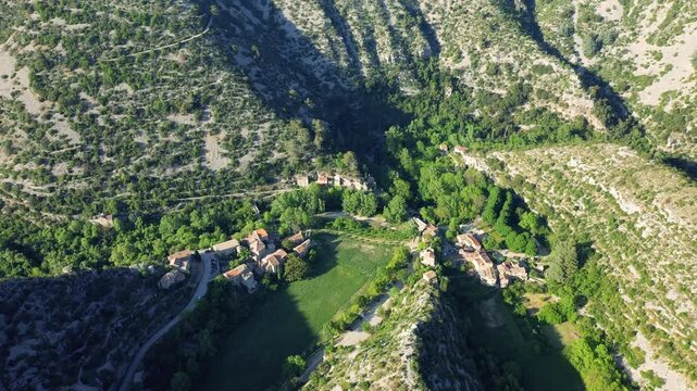 A high-angle aerial shot of the picturesque village of Navacelles, nestled within the dramatic limestone canyon of the Cirque de Navacelles in southern France.