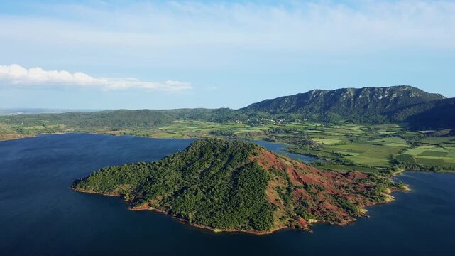 Aerial footage of Lac de Salagou in Herault, Occitanie, France, featuring a striking peninsula with red soil and lush green vegetation surrounded by deep blue lake water.