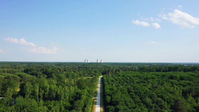 Aerial drone footage showing a straight road cutting through dense green forest, leading towards the Dampierre-en-Burly nuclear power plant in the distance. No people are visible in the scene.