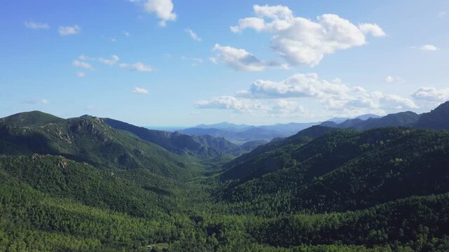 Aerial panoramic footage showcasing the lush green mountains and rolling hills surrounding the town of Baunei in Sardinia, Italy.