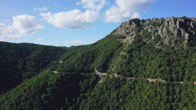 Drone footage capturing the lush green hills and rugged rocky cliffs in the countryside surrounding Baunei, Sardinia, Italy.