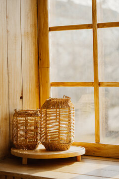 Two wicker lanterns on wooden windowsill against blurred autumn forest background. Warm natural light and cozy rustic atmosphere of fall interior design, natural materials, home decor