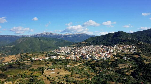 Wide aerial footage showcasing the town of Orosei nestled among lush green hills and mountains in Sardinia, Italy. No people are visible in the scene.